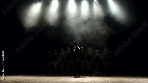 The choreographer teaches children the ballet on stage in the dark. Silhouette of choreographer and group of children dancing on stage on a black background. Theatrical bow. photo