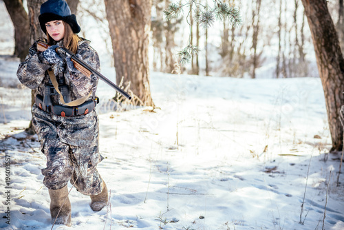 A beautiful hunter in a camouflage suit walks through the woods with weapons  preparing to hunt.