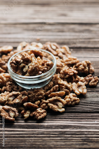 Pile of shelled walnuts in glass small bowl on wooden background, healthy eating concept