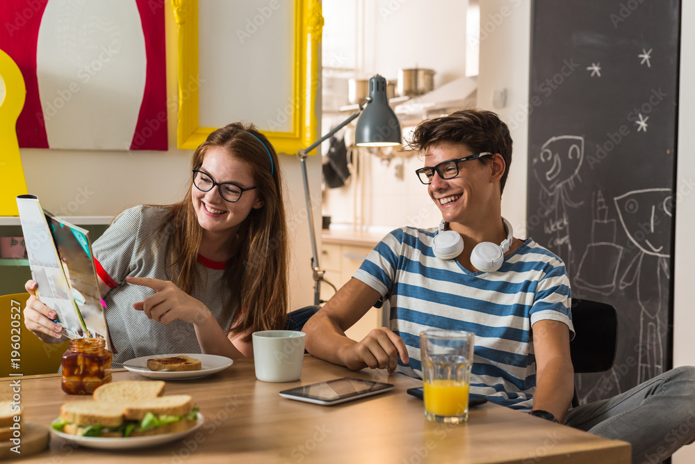 Teenage brother and sister watching the magazine while having breakfast at theirs home Teenage brother and sister watching the magazine while having breakfast at theirs home