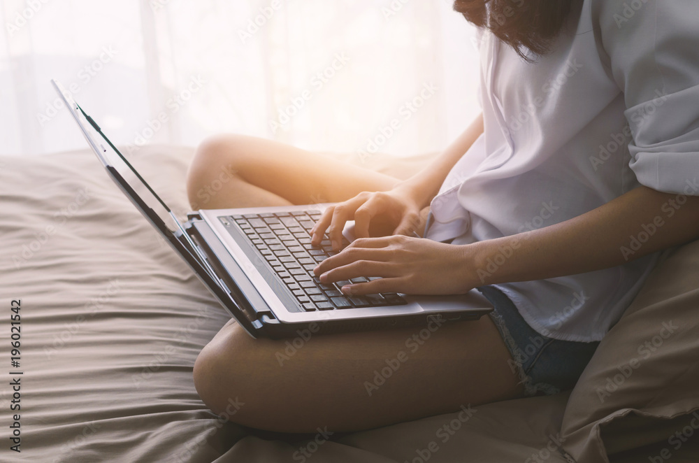 Naklejka premium attractive woman hands using laptop working typing keyboard on the bed in sleeping room at morning after wake up.