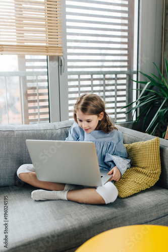 Little girl sitting on the couch and using laptop 