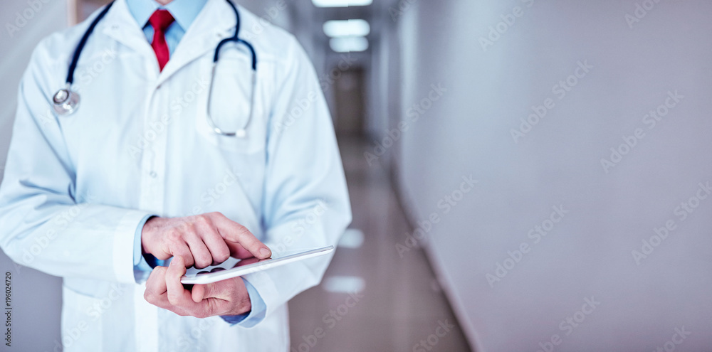 doctor in white medical coat is using a tablet and smiling while standing against window doctor in white medical coat is using a tablet and smiling while standing against window