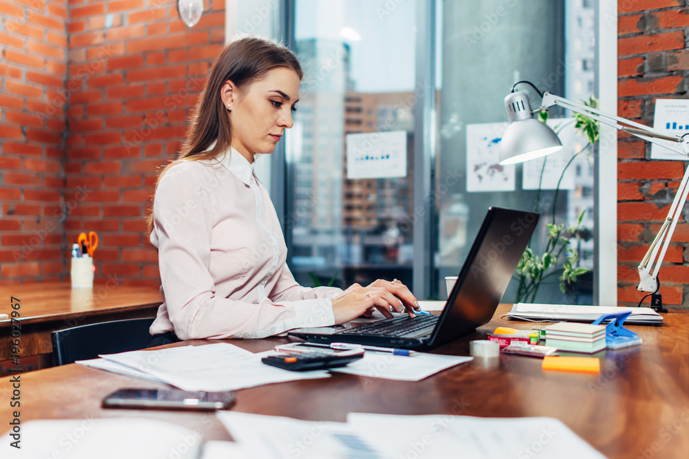 Young female wearing formal clothes working on laptop typing emails sitting at her workplace Young female wearing formal clothes working on laptop typing emails sitting at her workplace
