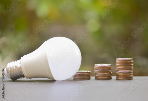 LED Bulb and Coin stack with green glass background for saving concept