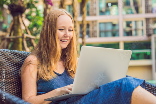 Young female freelancer sitting near the pool with her laptop in the hotel browsing in her smartphone. Busy at holidays. Distant work concept. Copy space for your text photo