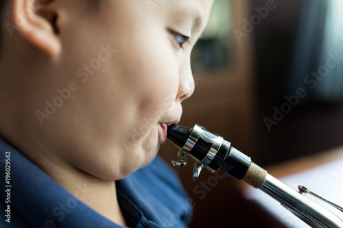 Asian kid practises saxophone with close up portrait style