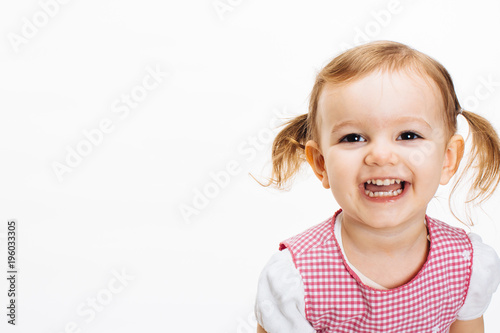 A very happy and excited toddler girl with ponytails laughing and showing teeth, isolated on white studio background