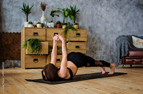 Young attractive smiling woman practicing yoga, stretching in Scorpion exercise, variation of vrischikasana  photo