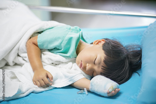 Sick child boy lying in bed with a fever, resting, IV solution in a child's patients hand
