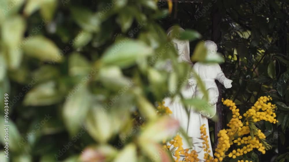 Slow motion shot panning right to reveal a stone statue of the Virgin Mary holding Baby Jesus in a bush in a garden in Rome Slow motion shot panning right to reveal a stone statue of the Virgin Mary holding Baby Jesus in a bush in a garden in Rome