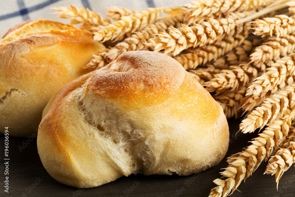Bunch of whole, fresh baked wheat buns with wheat ears on dark wooden table