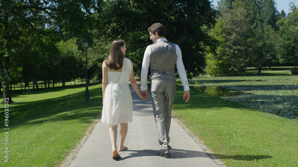 CLOSE UP: Young happy couple holding hands gaze at each other walking in park CLOSE UP: Young happy couple holding hands gaze at each other walking in park