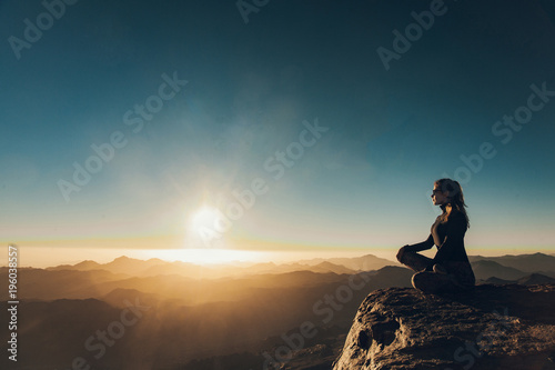 Woman sits in a pose of yoga on Mount Sinai and meditates against background of sunrise.