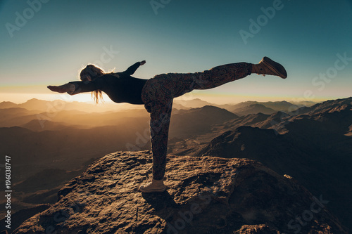 Woman does yoga exercises on cliff on Mount Sinai against background of sunrise.