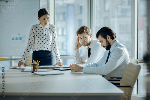 Shame on you. Strict young female boss frowning at her employees and scolding them in her office while they looking guilty and averting gaze