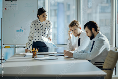 Bad job. Angry female boss having a meeting with her employees and reprimanding them for the poor performance while they looking embarrassed photo