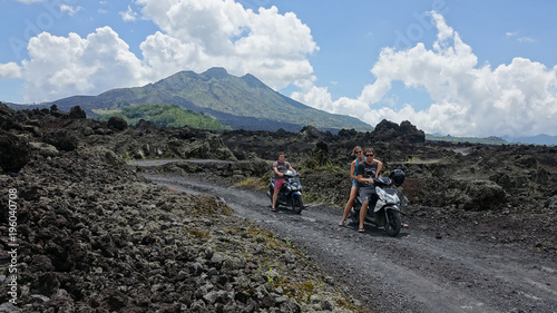 Three friends on a fun scooter trip taking a picture in front of large volcano