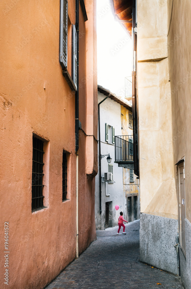 Boy in pink clothes holding pink balloon celebrates Breast Cancer Awareness Month in October in narrow Italian street in Chiavenna, Italy