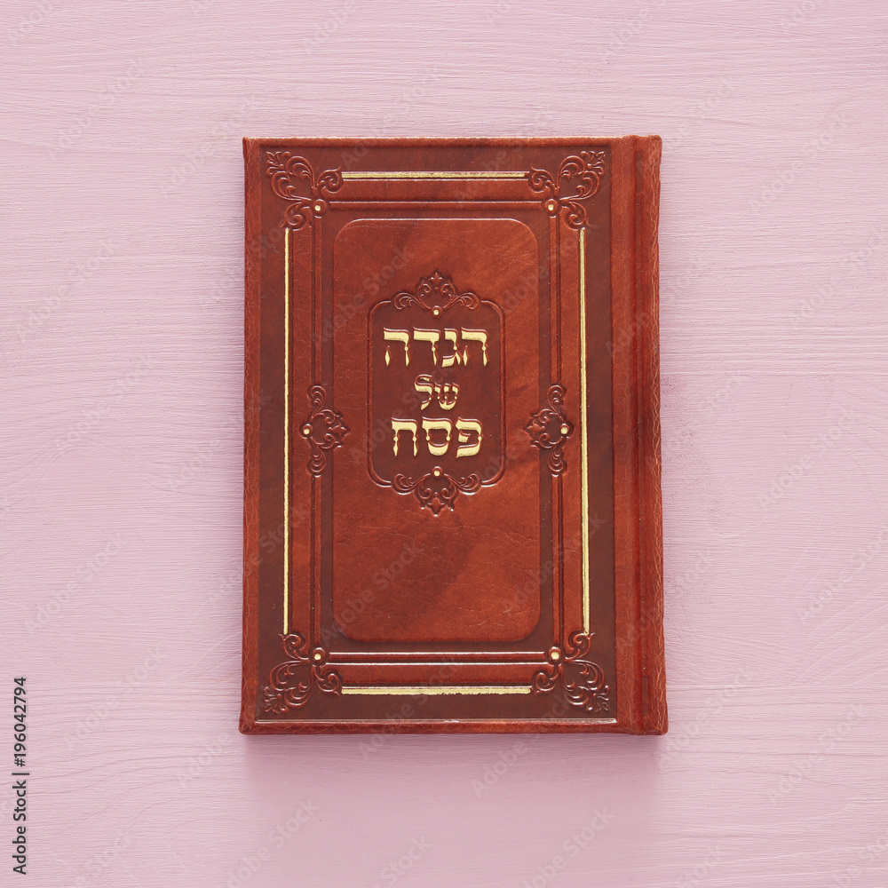 Fototapeta premium Pesah celebration concept (jewish Passover holiday). Traditional book with text in hebrew: Passover Haggadah (Passover Tale).
