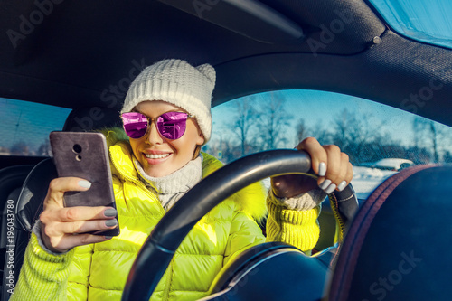 красивая молодая женщина за рулем автомобиля и смотрит в смартфон 