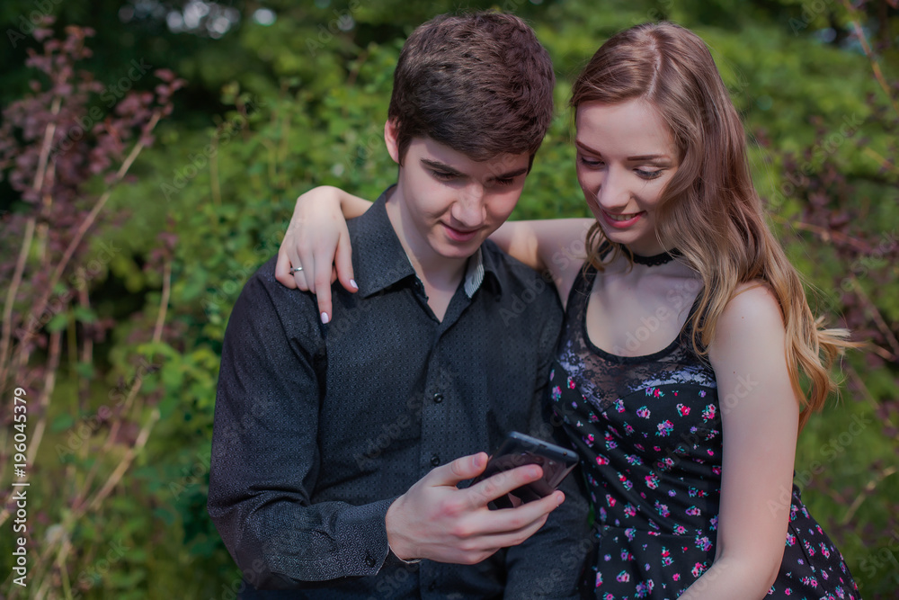 guy with a girlfriend makes a selfie in nature. young man with beautiful girl is looking at the screen of black phone. guy with a girlfriend makes a selfie in nature. young man with beautiful girl is looking at the screen of black phone.