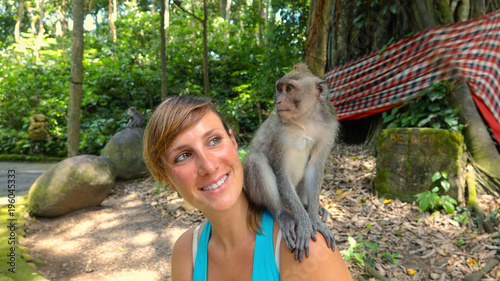 Canvas Print CLOSE UP: Young Caucasian traveler looking at little macaque on her shoulder