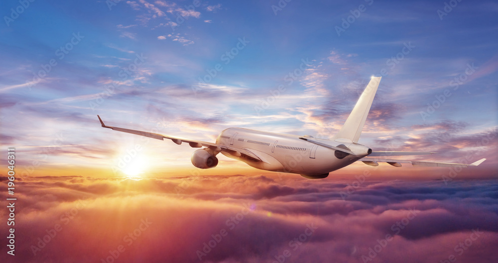 Big commercial airplane flying above clouds in sunset