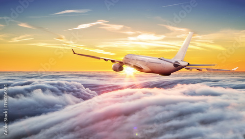 Big commercial airplane flying above clouds in sunset