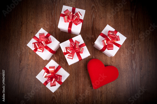 white festive gift boxes with red bows on a wooden table with red heart