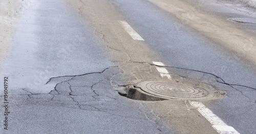 Pothole in asphalt near the sewer hatch, in the middle of the street