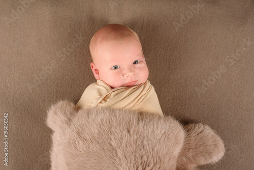 A cute little neborn baby is looking into the camera. The neborn baby could be a boy or girl and has blue eyes. parenting or love concept. photo