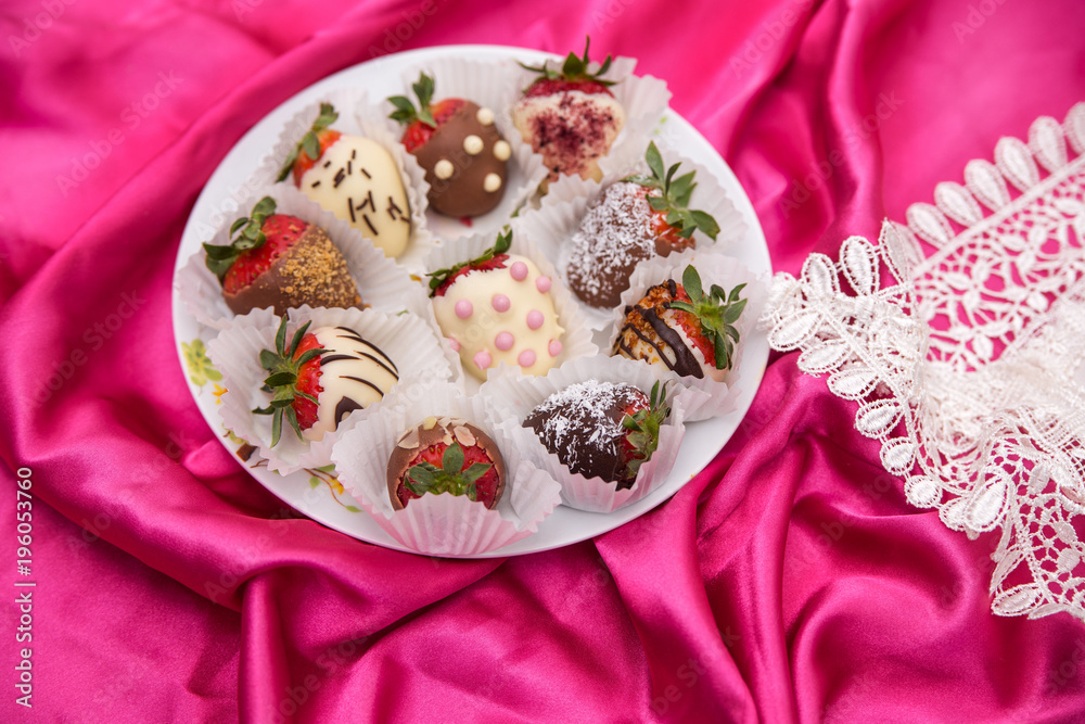 plate of Strawberries in white and milk chocolate on a pink silk background plate of Strawberries in white and milk chocolate on a pink silk background