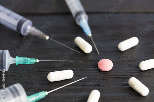 Medical syringes of various capacities, capsules, tablets lie on an old black wooden board.