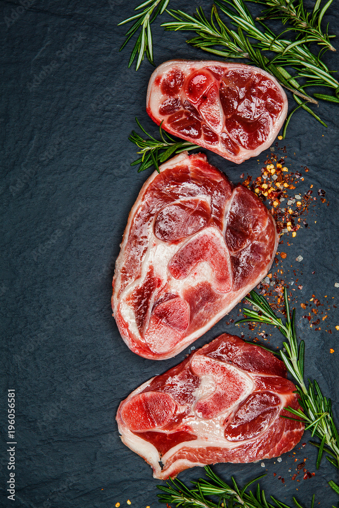 Raw juicy meat steaks ready for roasting and vegatables on a black board background. Space for text
