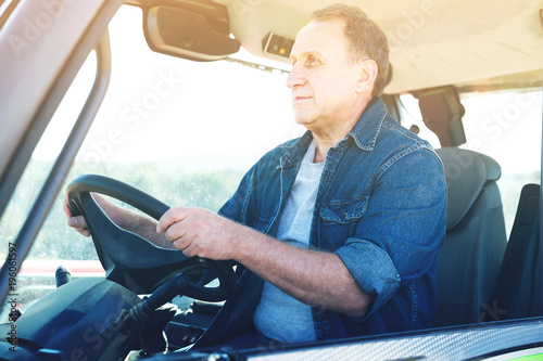 mature farmer is sitting on the car at the cowfarm photo