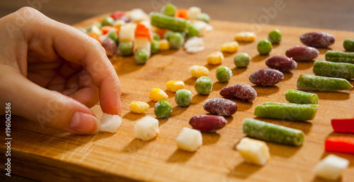 woman's hand collects even row of colorful Frozen mixed vegetables on a wooden background. top view photo
