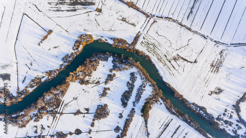 Aerial view riverbend passing snow covered fields. photo