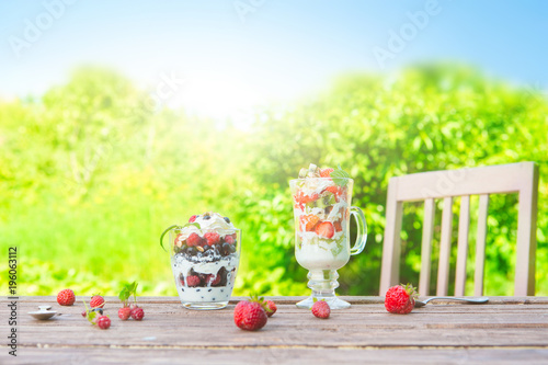 Layered dessert with raspberry, strawberry, black currant and kiwi, cream and biscuits in glasses photo