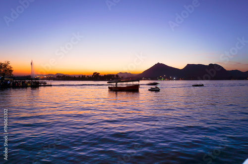 Boats on the famous pichola lake in Udaipur at sunset. This colorful shot shows mountains in the distance a beautiful sky and beautiful blue tones of this famous tourist place
