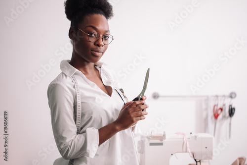 smiling african seamstress looking at camera with sewing machine photo