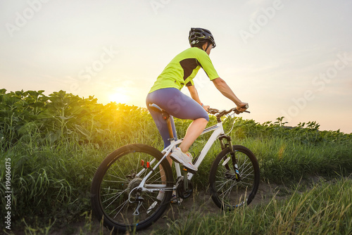 a woman is riding a bicycle between fields in the summer at sunset