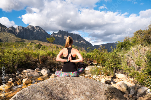 female performing yoga pose with scenic mountain and river background