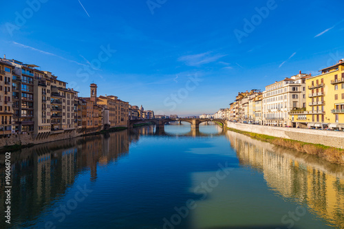 Cityscape view on Arno river with famous Holy Trinity bridge in Florence. Reflections on water. Old colorful houses on the side. Tuscany, Italy