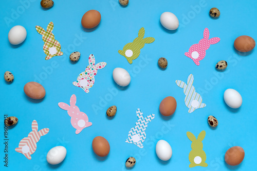 Easter bunny decoration and eggs on blue background, copy space. DIY holiday handicraft of colorful rabbits. Flat lay, top view. Paper rabbits cutouts. Easter greeting card. Happy Easter concept