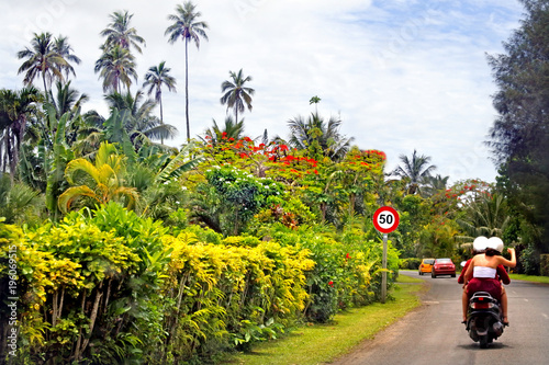 Tourist ride scooters on Rarotonga coastal ring road in the Cook Islands