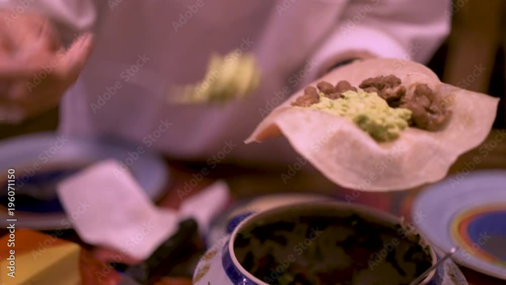 Closeup shot of someone making a burrito with refried pinto beans and putting avocado onto it while holding it in her hand.. Closeup shot of someone making a burrito with refried pinto beans and putting avocado onto it while holding it in her hand..