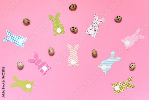 Easter bunny decoration and eggs on pink background, copy space. DIY holiday handicraft of colorful rabbits. Flat lay, top view. Paper rabbits cutouts. Easter greeting card. Happy Easter concept