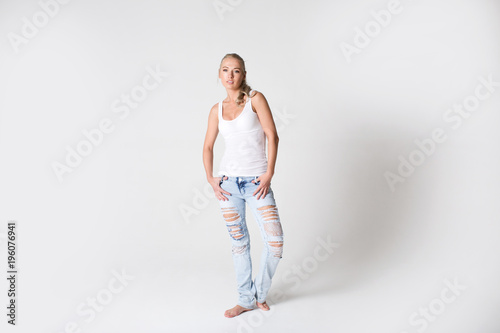 Young modern smiling woman in jeans and a T-shirt on a gray background.