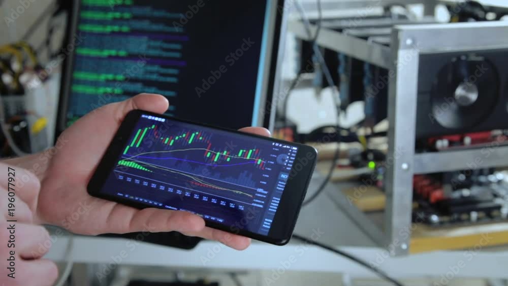 Crop shot in close-up of miner showing smartphone with cryptocurrency rate.